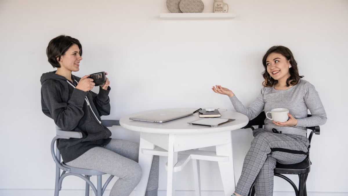 Two women enjoying a friendly chat over coffee indoors, relaxed and smiling.